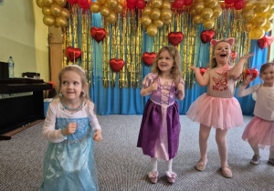 Dziewczynki przebrane za Elzę, księżniczkę, kotka i motylka tańczą stojąc obok siebie