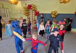 Dzieci w strojach karnawałowych trzymają się za ręce tworząc długiego węża