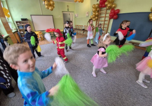 Dzieci przebrane w stroje karnawałowe tańczą trzymając w dłoniach kolorowe pompony