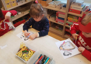 Dzieci siedzą przy stole i kolorują obrazki z pingwinami