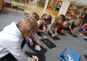 Dzieci siedzą na dywanie i wykonują wydzierankę z pingwinem