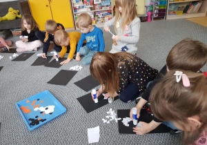 Dzieci siedzą na dywanie i wykonują wydzierankę z pingwinem