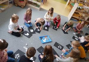 Dzieci siedzą na dywanie i wykonują wydzierankę z pingwinem