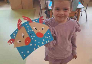 Dziewczynka pozuje do zdjęcia ze swoją pracą plastyczną przedstawiającą renifery