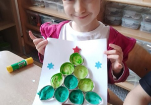Dziewczynka prezentuje wykonaną przez siebie pracę plastyczną pt. "Choinka"