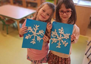 Dziewczynki pozują do zdjęcia ze swoją pracą plastyczną przedstawiającą śnieżynkę wyklejoną z folii aluminiowej