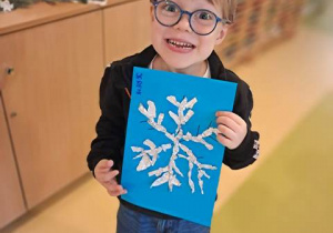 Jeremi pozuje do zdjęcia ze swoją pracą plastyczną przedstawiającą śnieżynkę wyklejoną z folii aluminiowej