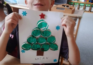 Chłopiec prezentuje wykonaną przez siebie pracę plastyczną pt. "Choinka"