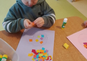 Chłopiec dokleja elementy bibuły do kartki papieru