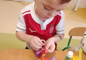 Chłopiec siedzi przy stole i skleja kolorowe paski papieru tworząc łańcuch na choinkę