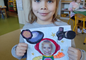 Dziewczynka prezentuje pracę plastyczną: ,,Ja w kosmosie".
