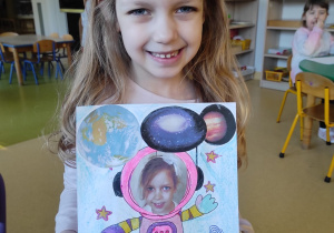 Dziewczynka prezentuje pracę plastyczną: ,,Ja w kosmosie".