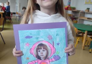 Dziewczynka prezentuje pracę plastyczną: ,,Ja w kosmosie".