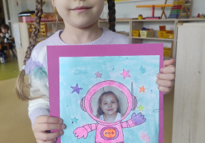 Dziewczynka prezentuje pracę plastyczną: ,,Ja w kosmosie".