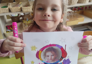 Dziewczynka prezentuje pracę plastyczną: ,,Ja w kosmosie".