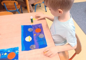 Jasio przykleja planety na niebieską kartkę papieru