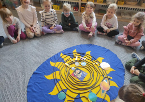 Dzieci siedzą w kręgu i oglądają makietę z Układem Słonecznym.