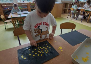 Chłopiec w czasie wykonywania pracy plastycznej dokleja papierowe gwiazdy do czarnego arkuszu papieru