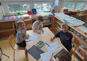 Dzieci przy stoliku kreślą po śladzie astronautę z wykorzystaniem mazaków