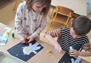 Dziewczynka i chłopiec doklejają papierowe gwiazdki do ciemnego arkuszu