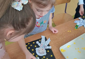 Dziewczynka posypuje swoją pracę plastyczną pt. "Astronauta w galaktyce" brokatem