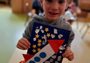 Brunon prezentuje wykonaną przez siebie pracę plastyczną przedstawiającą rakietę kosmiczną