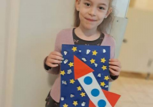 Dziewczynka trzyma w dłoniach wykonaną przez siebie pracę plastyczną pt. "Podróż w kosmos"
