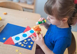 Dziewczynka podczas wykonywania pracy plastycznej pt. "Podróż w kosmos" wypełnia tło poprzez doklejenie papierowych gwiazdek