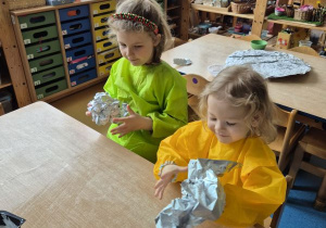 Dziewczynki siedzą przy stoliku i zgniatają folię aluminiową w kulki