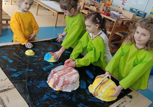 Dzieci przyklejają planety do pomalowanego na czarno kartonu w dużym formacie