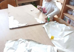 Dziewczynka przykleja folię aluminiową na skrzydło rakiety