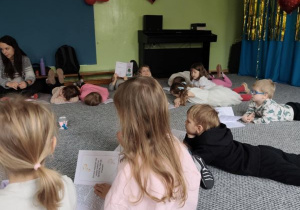 Dzieci siedzą i leżą na dywanie słuchając opowiadania o złości