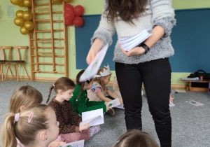 Prowadząca zajęcia rozdaje siedzącym w kręgu dzieciom książeczki