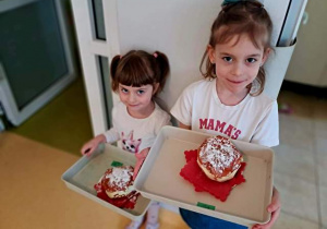 Maja i Tosia trzymają w dłoniach tace z pączkami zrobionymi podczas zabawy plastycznej