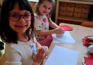 Ala i Jagoda podczas zabawy plastycznej pt. "Pączek" zgniatają kartki papieru w kulki