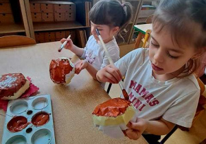 Dziewczynki malują brązową farbą kulki uformowane z kartek papieru