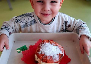 Chłopic pozuje do zdjęcia i trzyma w dłoniach tace ze swoją pracą plastyczną pt. "Pączek" wykonaną z papieru
