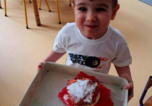 Chłopiec trzyma w dłoniach tace ze zrobionym przez siebie pączkiem w czasie zabawy plastycznej