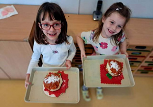 Dwie dziewczynki trzymają w dłoniach tace i prezentują wykonane przez siebie pączki