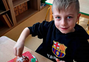 Chłopiec w czasie zabawy plastycznej posypuje pączka wykonanego z papieru białą posypką