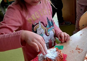 Dziewczynka w czasie pracy plastycznej posypuje pączka zrobionego z papieru posypką