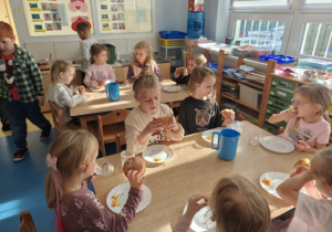 Dzieci siedzą przy stolikach i jedzą pączki