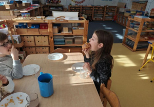 Dzieci siedzą przy stoliku i jedzą pączki