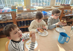 Dzieci siedzą przy stoliku i jedzą pączki