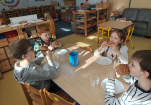 Dzieci siedzą przy stoliku i jedzą pączki