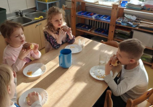 Dzieci siedzą przy stoliku i jedzą pączki