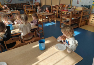 Dzieci siedzą przy stoliku i jedzą pączki