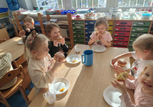 Dzieci siedzą przy stoliku i jedzą pączki