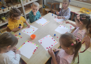 Dzieci naklejają kolorowe kwiatuszki na papierowe talerzyki.