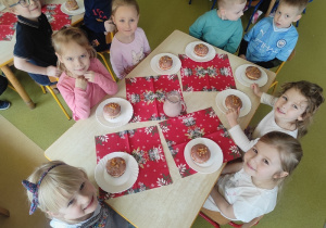 Dzieci siedzą przy stole i jedzą pączki.